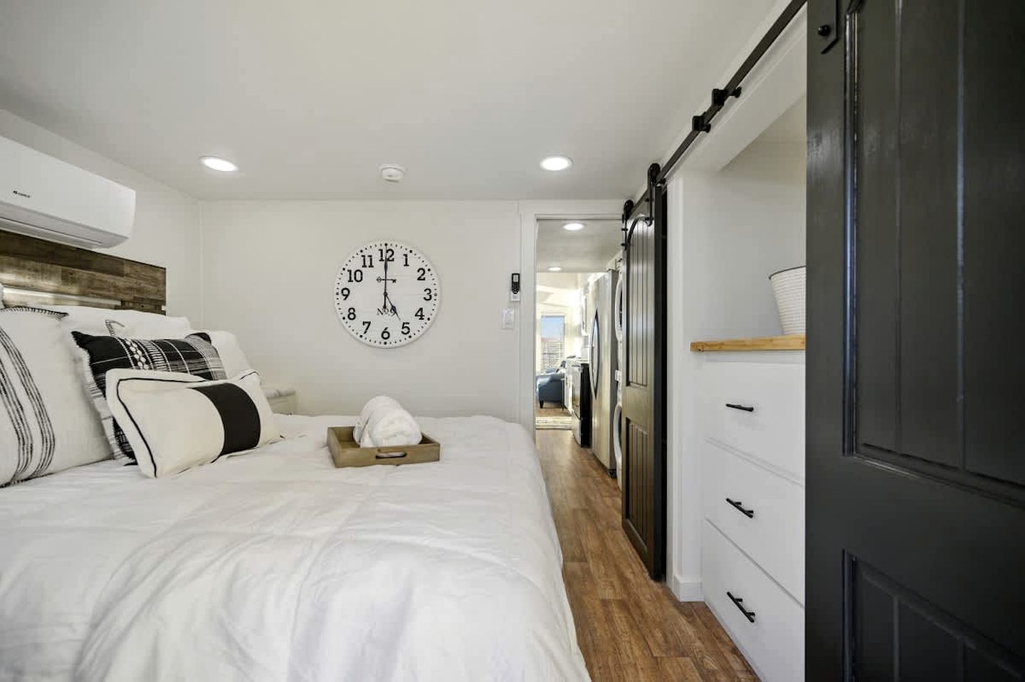 A bedroom with a bed, a clock, a wardrobe, and a laundry area.