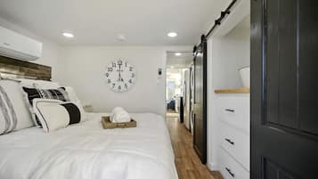 A bedroom with a bed, a clock, a wardrobe, and a laundry area.