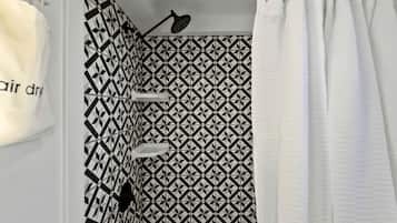 A bathroom with a geometric patterned tile wall, a shower curtain, and a handheld showerhead.