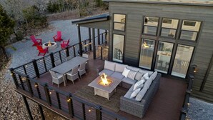 Eine Terrasse mit Gartenmöbeln, einer Feuerstelle und einem modernen Gebäude mit großen Fenstern.