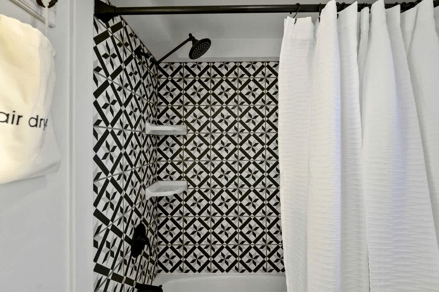 Un bagno con una parete rivestita di piastrelle a motivi geometrici, una tenda da doccia e un soffione manuale.