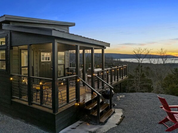A modern house with a deck, outdoor seating, and a view of the landscape.