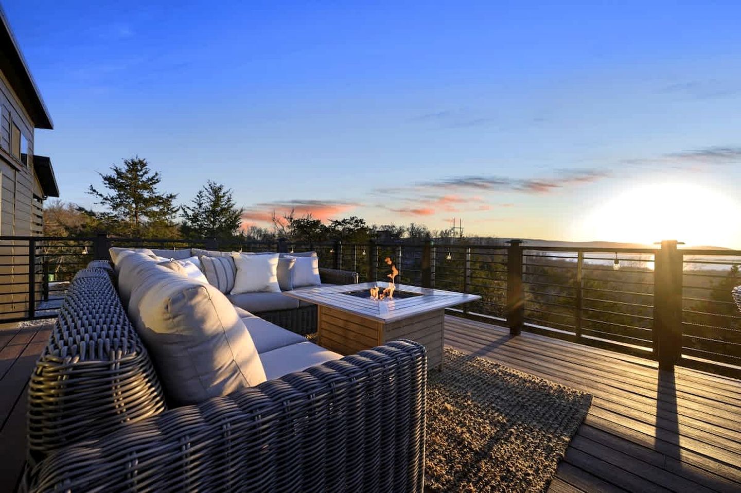 Eine Terrasse mit einem Korbsessel, einer Feuerstelle und Blick auf den Sonnenuntergang.