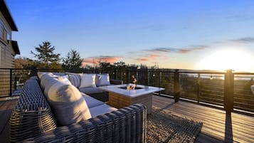 Eine Terrasse mit einem Korbsessel, einer Feuerstelle und Blick auf den Sonnenuntergang.