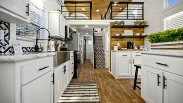 A modern kitchen with white cabinetry, a wooden ceiling, and a black and white patterned rug.