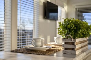 A table with a white cup and saucer, a potted plant, and a television mounted on the wall.