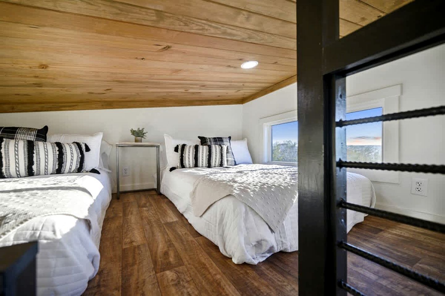 A bedroom with two beds, wooden flooring, a small bedside table with a plant, and a window with a view.