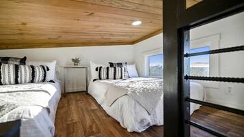 A bedroom with two beds, wooden flooring, a small bedside table with a plant, and a window with a view.