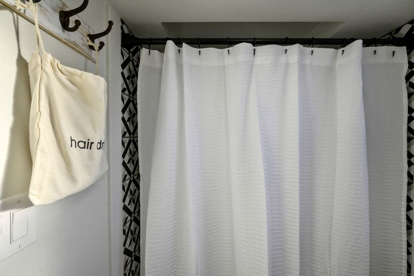 A bathroom with a white shower curtain, a beige towel, and a black and white patterned towel hanging on a rack.