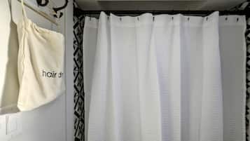 A bathroom with a white shower curtain, a beige towel, and a black and white patterned towel hanging on a rack.