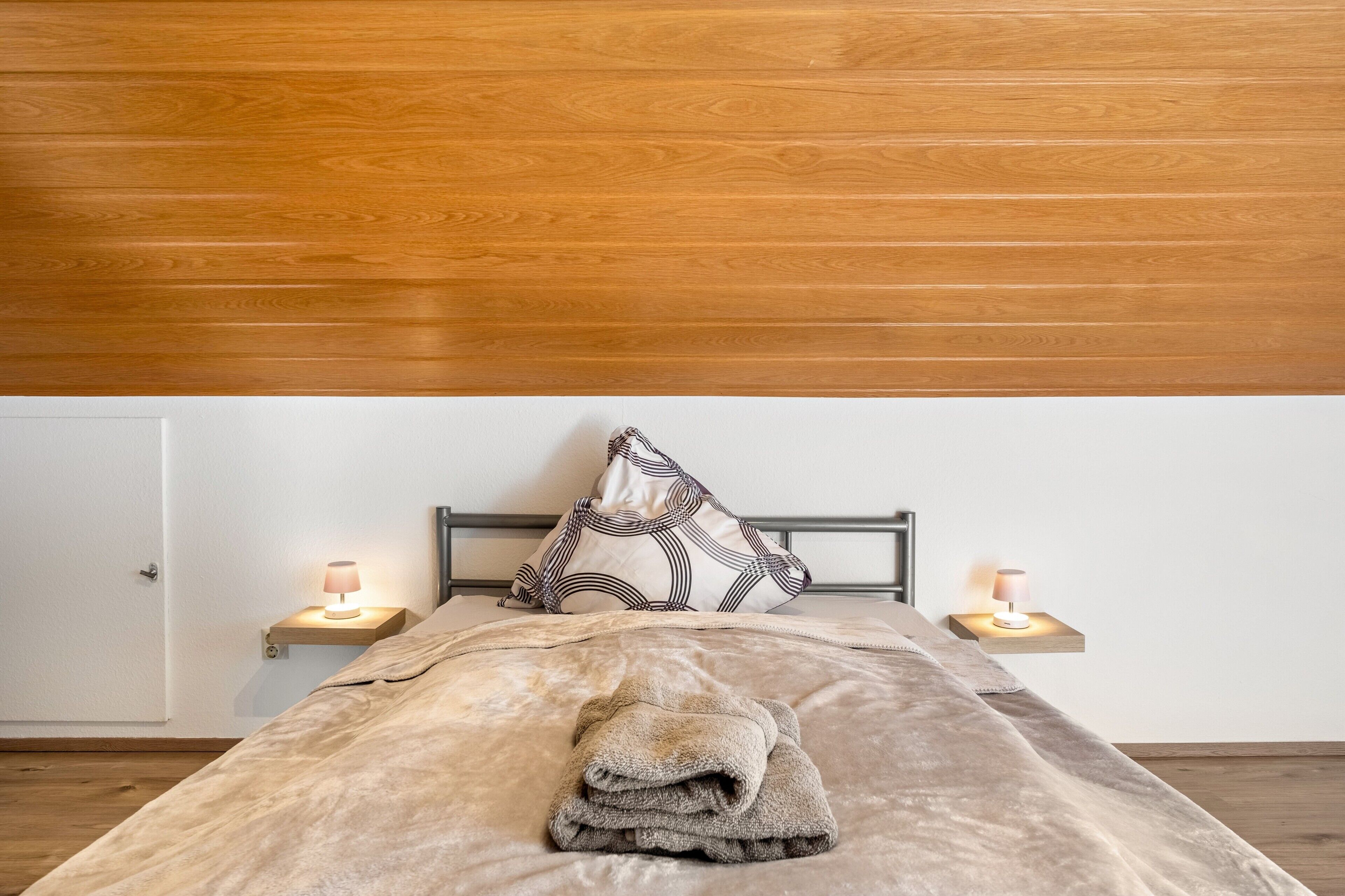 A bed with a folded towel, a patterned pillow, and two bedside lamps on wooden nightstands.