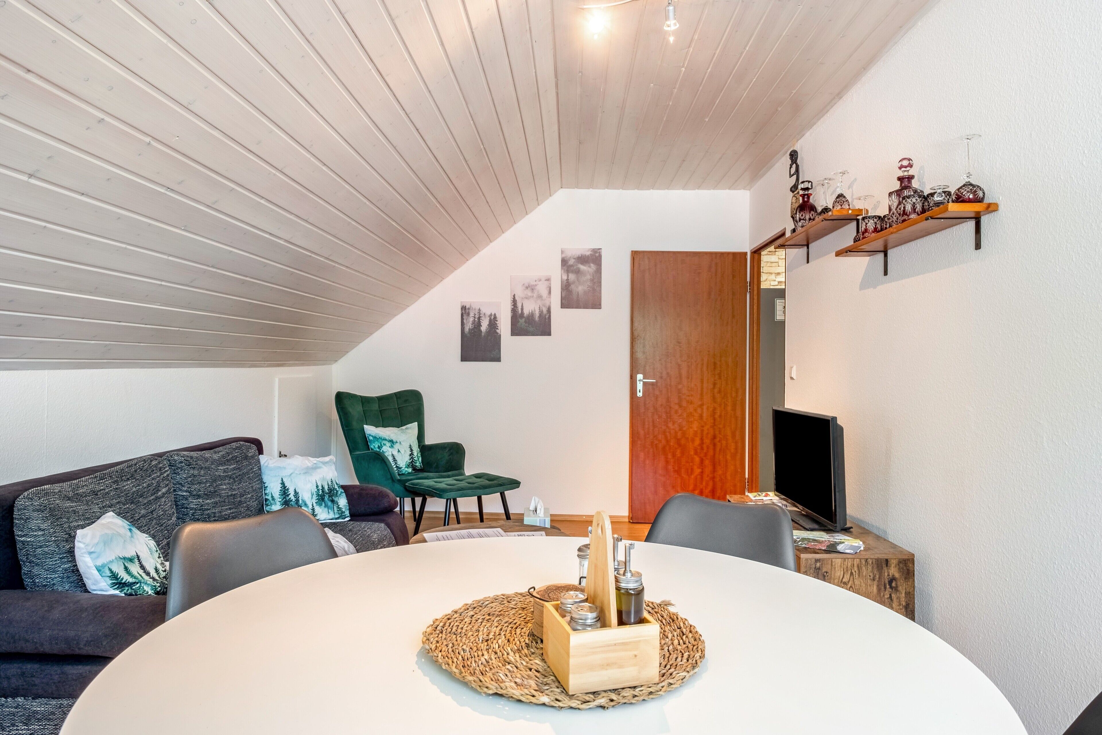 A modern living room with a round table, a green armchair, a sofa, and a TV.