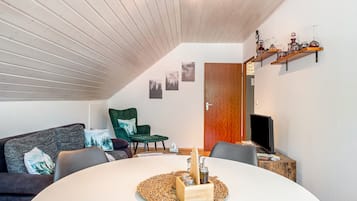 A modern living room with a round table, a green armchair, a sofa, and a TV.