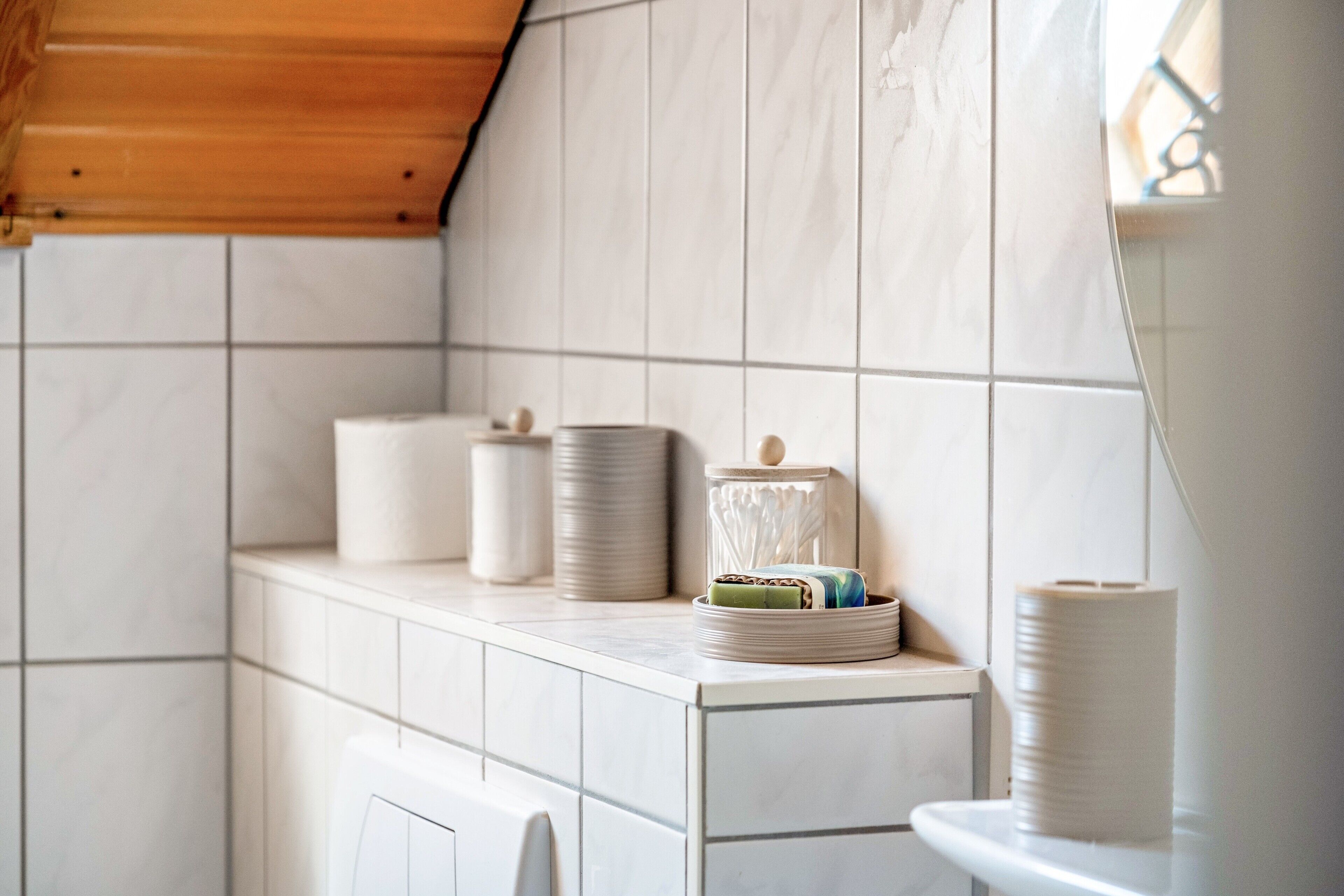 A bathroom with white tiles, a wooden ceiling, and a toilet.