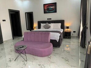 Ein modernes Schlafzimmer mit einem Bett, einem violetten Sofa, einem kleinen Tisch und einem Bild an der Wand.