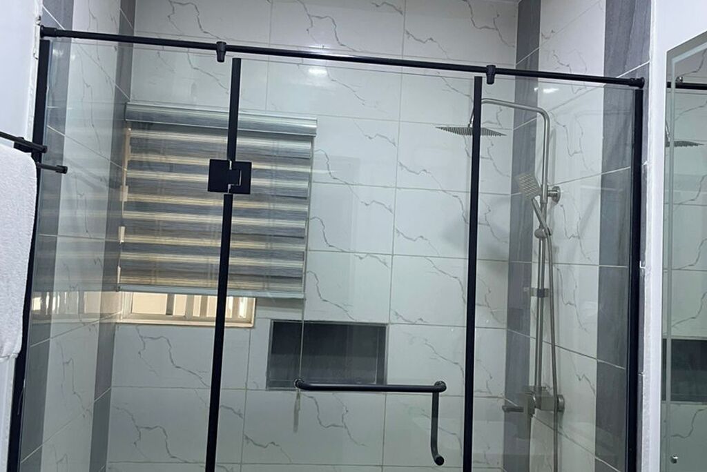 Un área de ducha con paredes de vidrio, una puerta metálica, una ventana pequeña y un pasamanos.