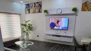 Una sala de estar con televisión de pantalla plana, un sofá, una mesa de centro, una planta en maceta y obras de arte en la pared.