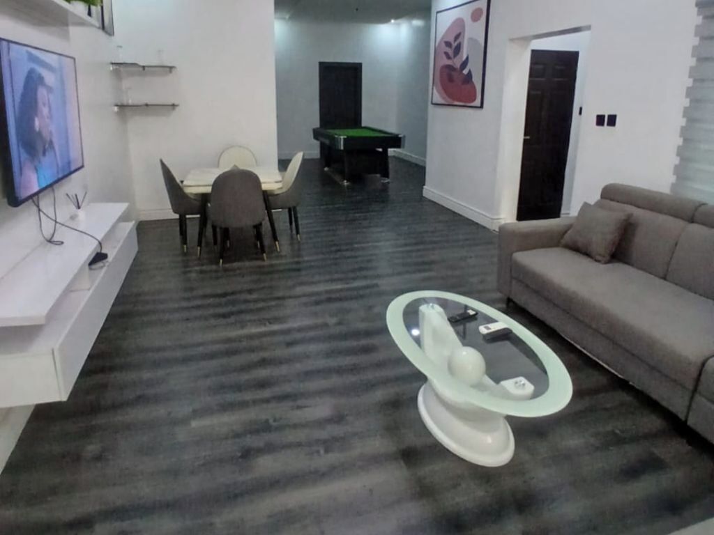 A living room with a pool table, a sofa, a TV, and a glass coffee table.