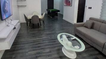 A living room with a pool table, a sofa, a TV, and a glass coffee table.