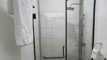 A glass-enclosed shower with a handheld showerhead, a towel rack, and a glass door.
