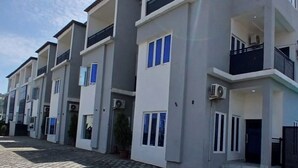 Una hilera de edificios residenciales modernos de varios pisos, con balcones, unidades de aire acondicionado y un camino pavimentado.