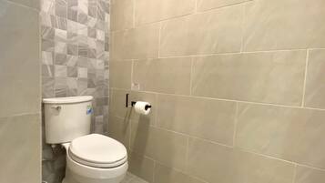 A bathroom with a toilet, a toilet paper holder, and a tiled wall.