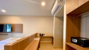 Habitación de hotel con escritorio de madera, cama, unidad de aire acondicionado, televisor y caja fuerte digital.