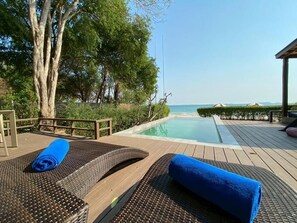 Una terraza de madera con sillones de descanso y una piscina.