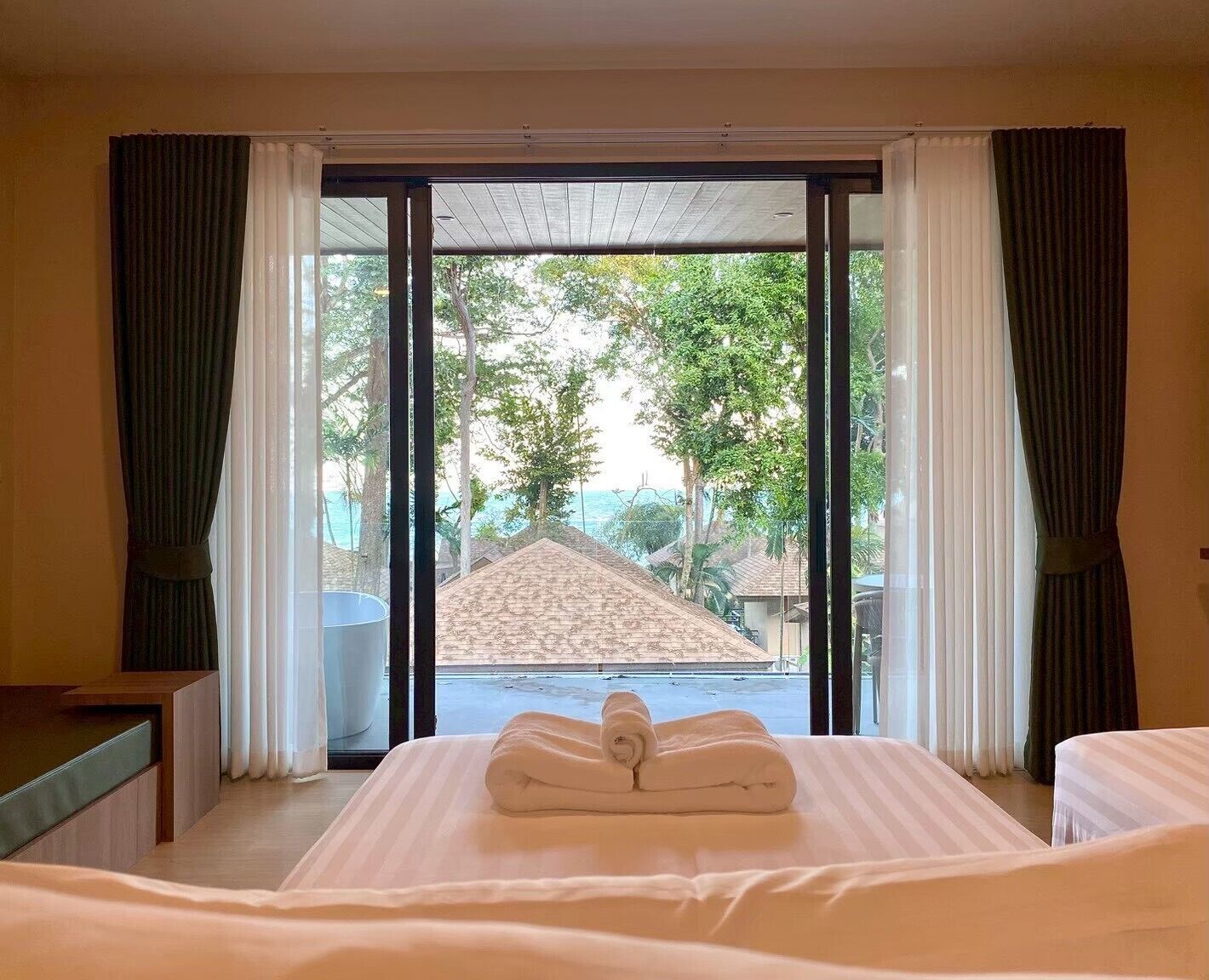A hotel room with a bed, a window with curtains, and a view of a building and trees outside.