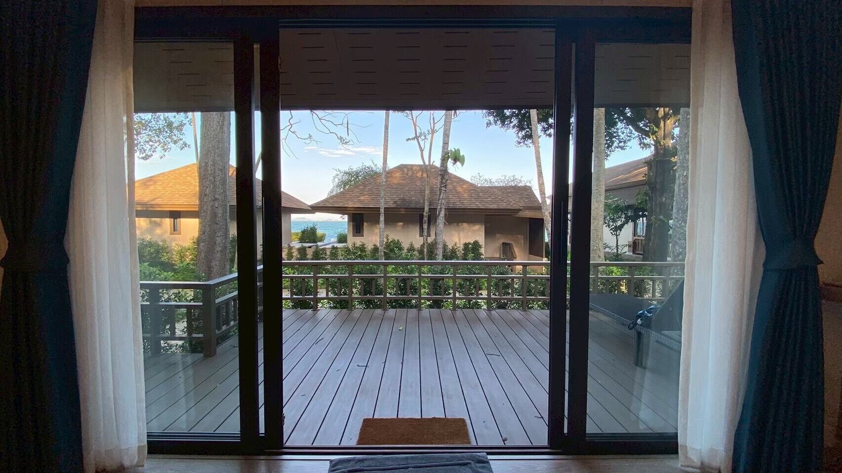 Vista desde una habitación con puerta corrediza de vidrio a una terraza de madera.