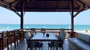 A covered outdoor seating area with a view of the sea, wooden furniture, and a table.