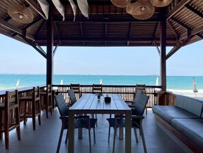 Un espacio de estar techado al aire libre con vista al mar, muebles de madera y una mesa.