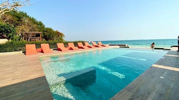 Une piscine à l’eau d’un bleu cristallin, entourée d’une terrasse en bois et de chaises longues rouges.