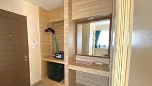 Una habitación con puerta de madera, un espejo, estante con un aspirador y un cesto de basura pequeño.