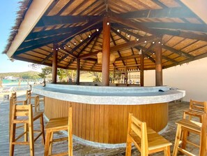 A wooden bar with a curved counter and bar stools, under a thatched roof structure. - Samed Amoris Resort & Pool Villas  (Bueang Sam Phan)