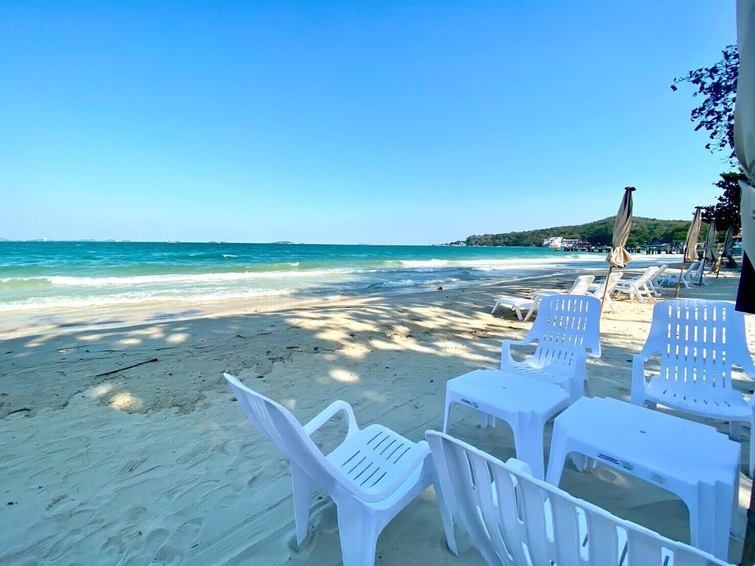 A beach with white plastic chairs and umbrellas, a clear sky, and a calm sea.