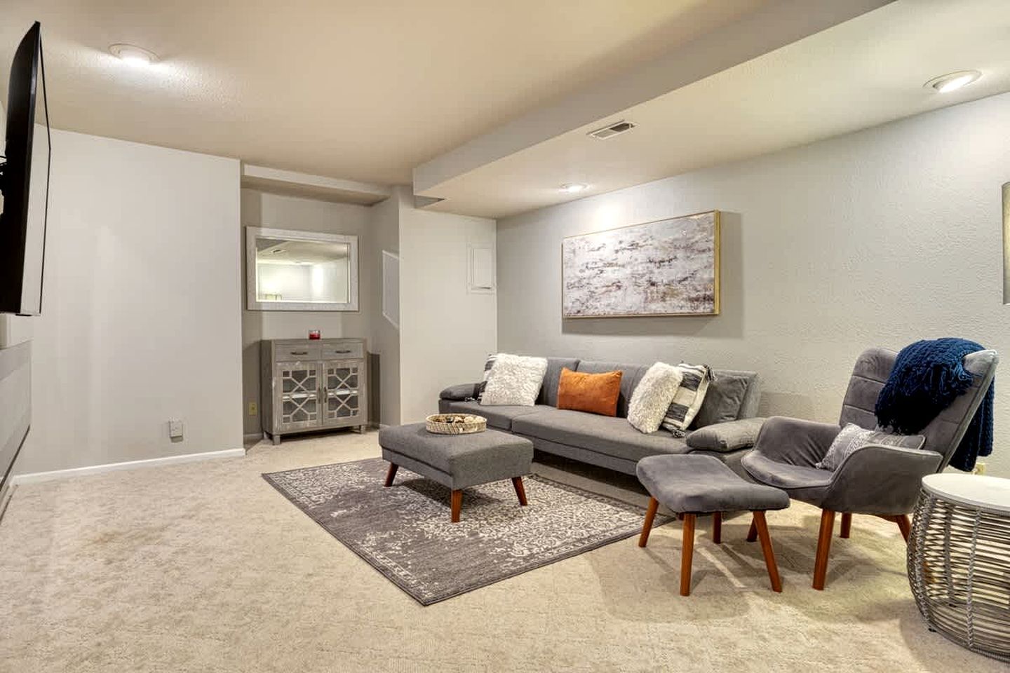 Un salon avec un canapé gris, deux fauteuils, une table basse, un tapis, un téléviseur, un meuble et un tableau accroché au mur.