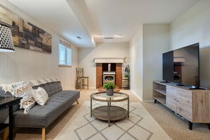 Un salon moderne avec un canapé gris, une table basse ronde, un téléviseur à écran plat et une cheminée.