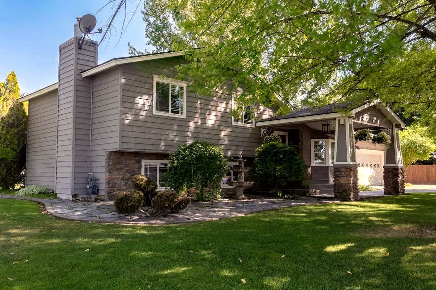 A two-story house with a stone chimney, a covered porch, and a well-maintained lawn.