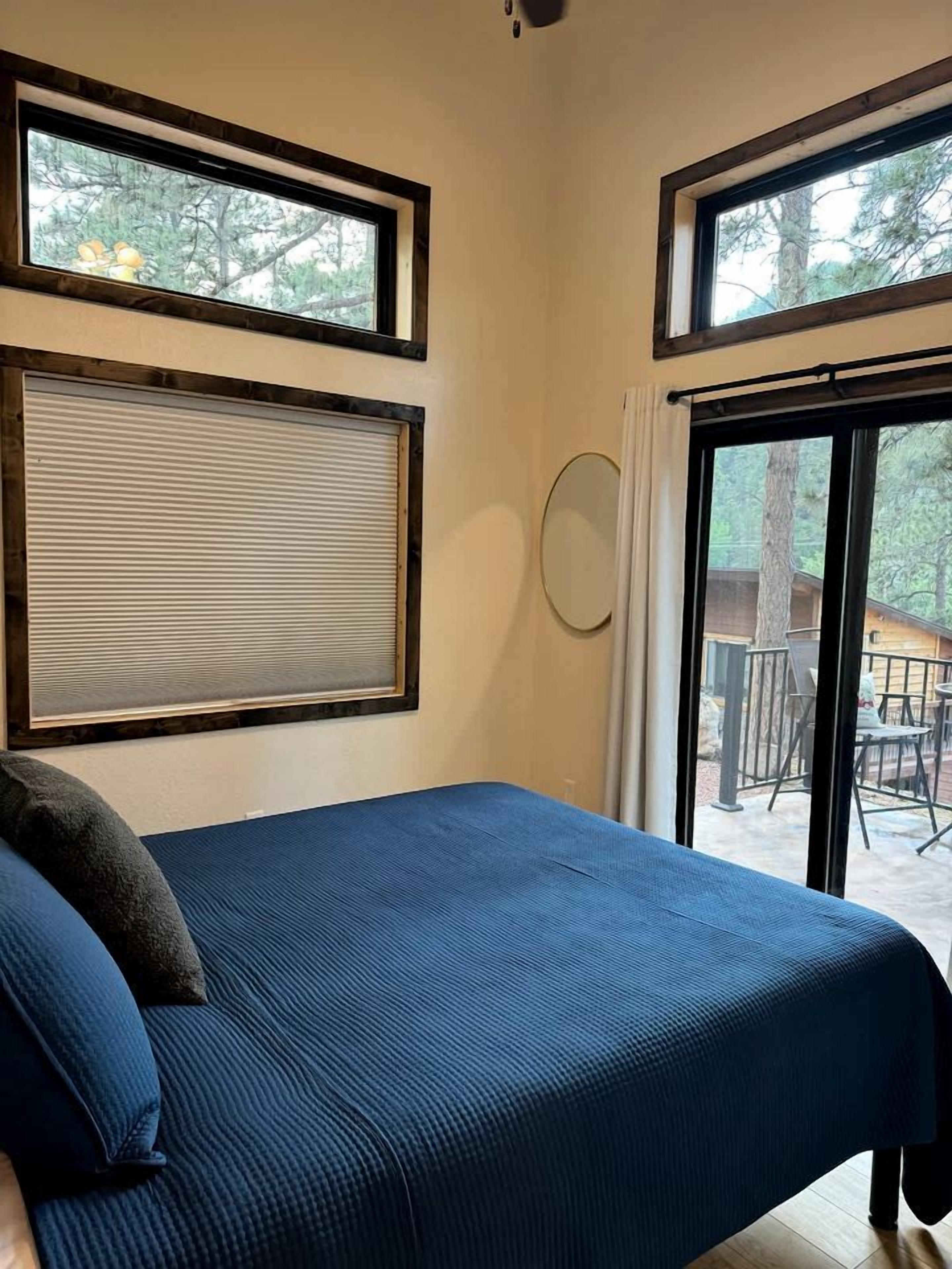 Ein Schlafzimmer mit einem Bett, zwei Fenstern und Blick ins Freie.