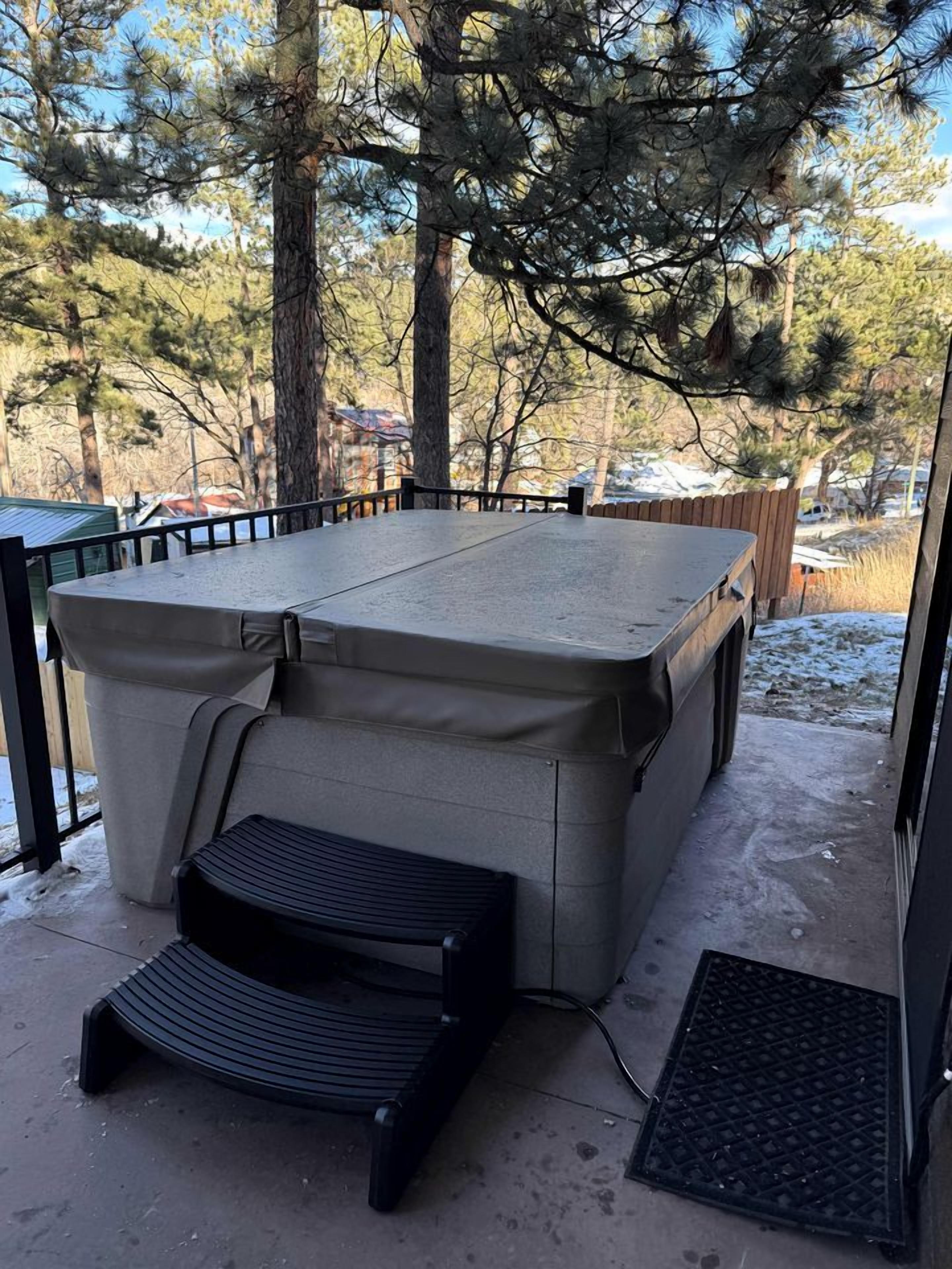 Un área de patio techada con una mesa y banco, rodeada de árboles y una valla de madera.