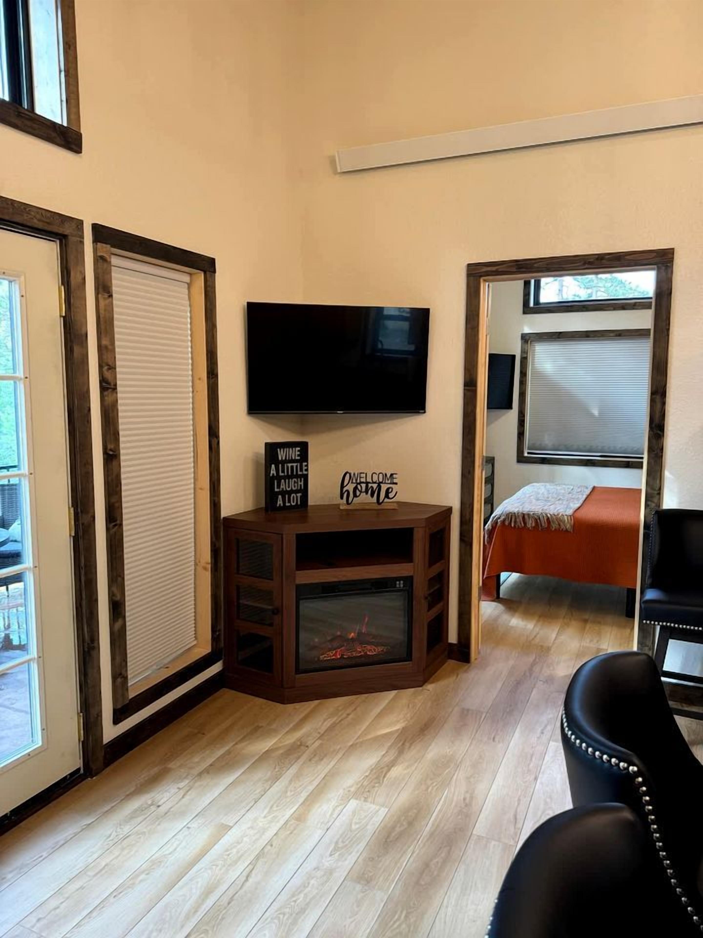 Ein Zimmer mit einem an der Wand befestigten Flachbildfernseher, einer kleinen Holztruhe mit Kamin und einem Bett mit orangefarbener Bettdecke sowie einem schwarzen Ledersessel.
