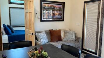 A room with a dining table, a sofa, a framed picture on the wall, and a door leading to another room.