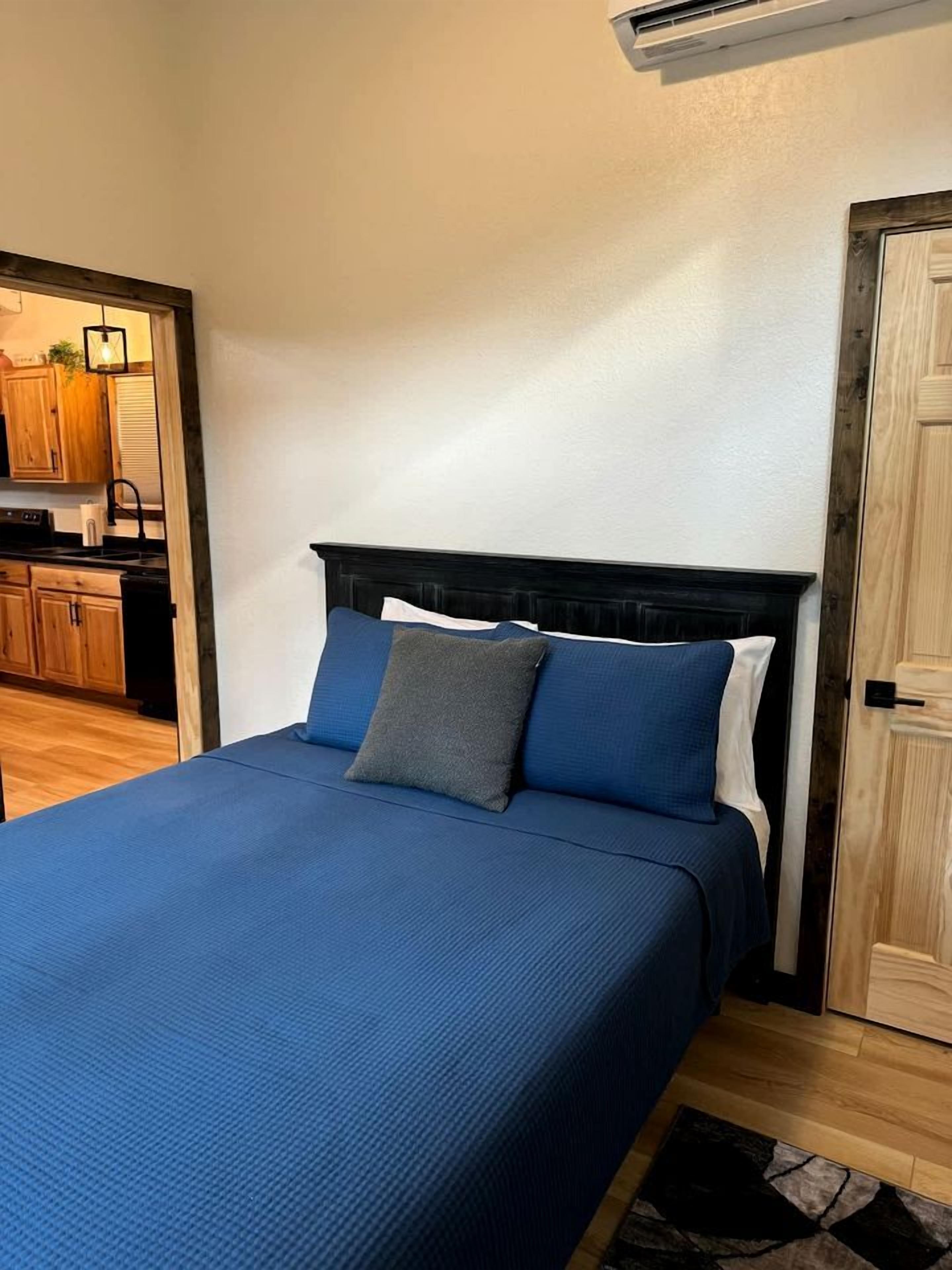 Une chambre à coucher avec un lit, une porte en bois et une cuisine visible à travers une porte ouverte.