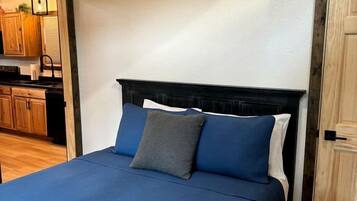 Une chambre à coucher avec un lit, une porte en bois et une cuisine visible à travers une porte ouverte.