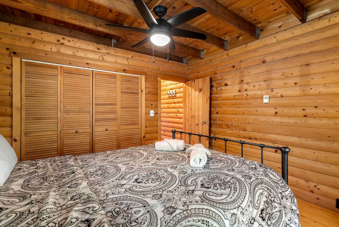 Ein Schlafzimmer in einer Holzhütte mit einem Bett, einem Deckenventilator und einem Schrank aus Holz.