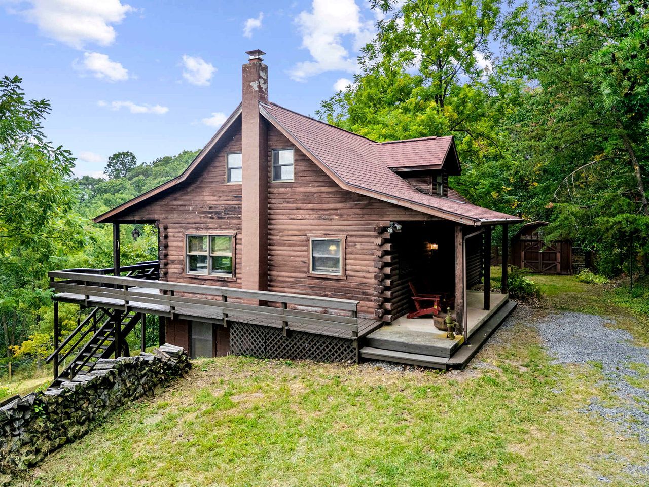 A rustic log cabin with a porch, a staircase, and a small outdoor area.