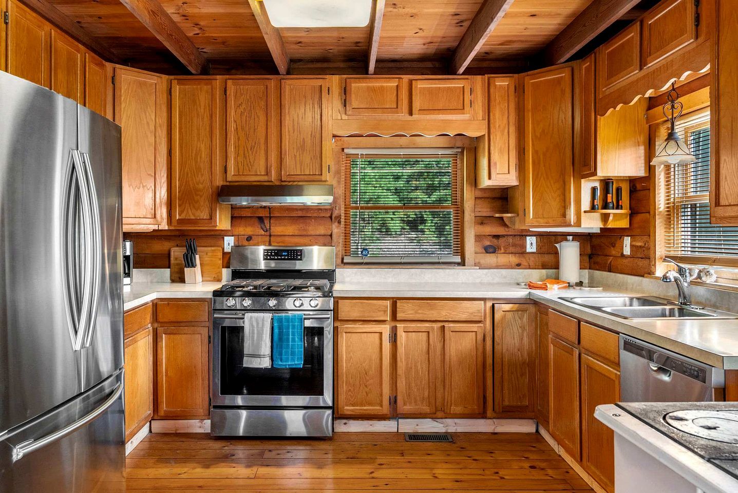Una cocina con gabinetes de madera, un refrigerador de acero inoxidable, una estufa y un lavamanos.