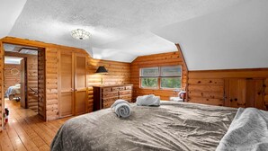 Un dormitorio de cabaña de madera con cama, cómoda y ventana.