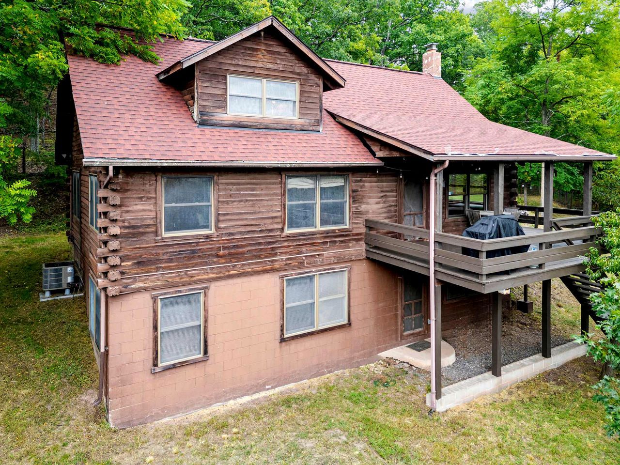 A two-story log cabin with a balcony, a chimney, and a small porch area.
